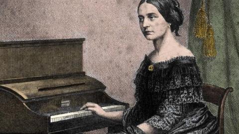 Der Komponist Robert Schumann steht neben seiner Ehefrau, der Pianistin und Komponistin Clara Schumann, sie sitzt am Klavier, er schaut sie an, sie schaut beiseite und scheint den Klängen nachzulauschen.