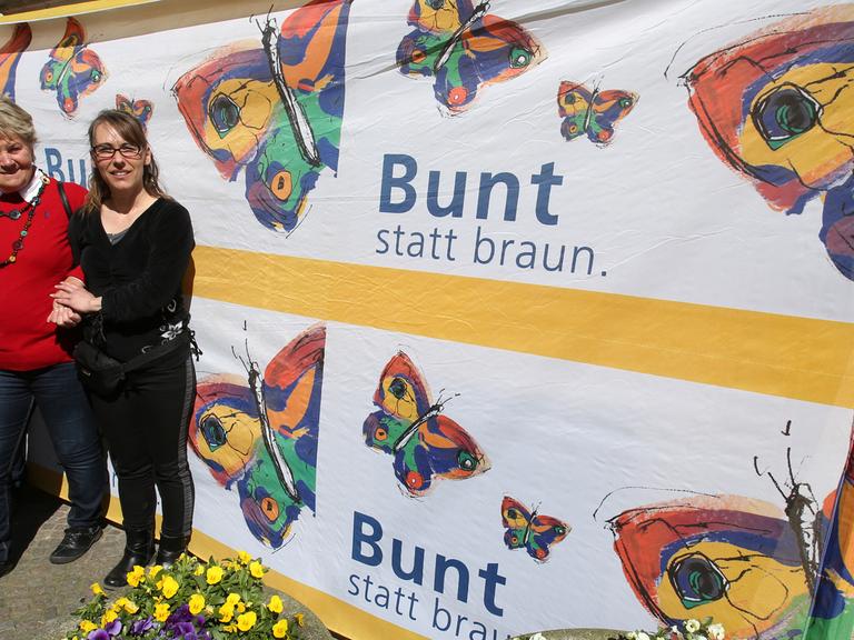 Vor der Villa Kunterbündnis in Güstrow (Mecklenbug-Vorpommern) steht am 19.04.2015 Geschäftsführerin Karen Larisch (r, Die Linke), um gemeinsam mit anderen gegen einen Aufmarsch der MVgida zu protestieren, auf dem Banner steht "Bunt statt braun".