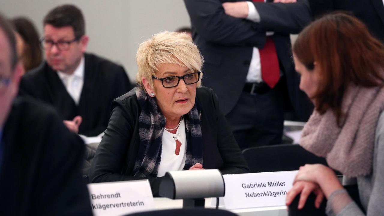 Die Nebenklägerin Gabi Müller sitzt in der Mitte des Bildes, rechts vor ihr steht eine weitere Frau. Müller, blonde Haare und Brillenträgerin, spricht mit dieser Frau. Die Nebenklägerin Gabi Müller sitzt in der Mitte des Bildes, rechts vor ihr steht eine weitere Frau. Müller, blonde Haare und Brillenträgerin, spricht mit dieser Frau.