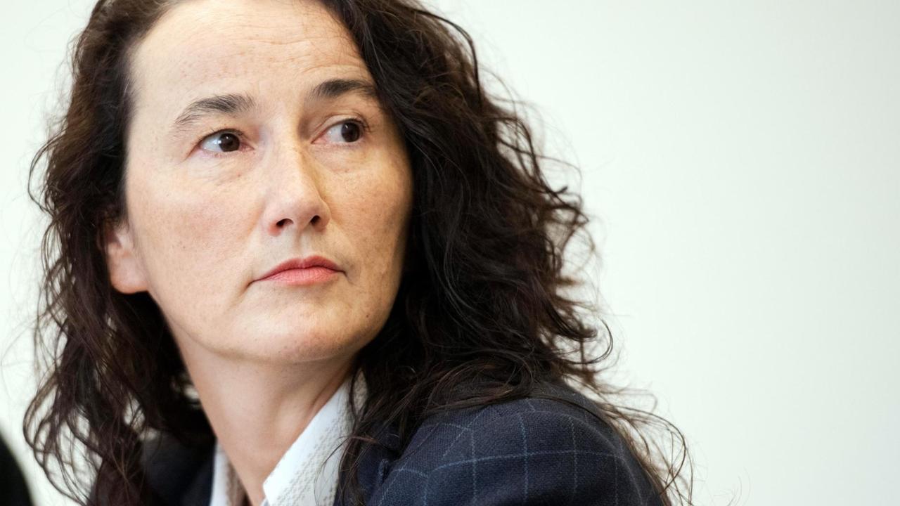 Eine Frau mit langen lockigen Haaren blickt ernst ins Off der Kamera. Eine Frau mit langen lockigen Haaren blickt ernst ins Off der Kamera.