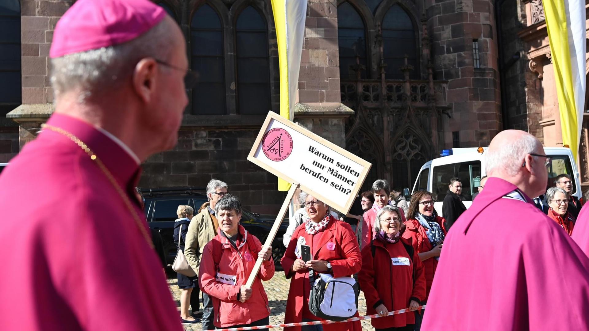 Priester laufen vor dem Münster an Teilnehmern einer Protestaktion der Initiative Maria 2.0 der Katholische Frauengemeinschaft in der Erzdiözese Freiburg vorbei. Auf einem Plakat steht "Warum sollen nur Männer berufen sein?". Priester laufen vor dem Münster an Teilnehmern einer Protestaktion der Initiative Maria 2.0 der Katholische Frauengemeinschaft in der Erzdiözese Freiburg vorbei. Auf einem Plakat steht "Warum sollen nur Männer berufen sein?".