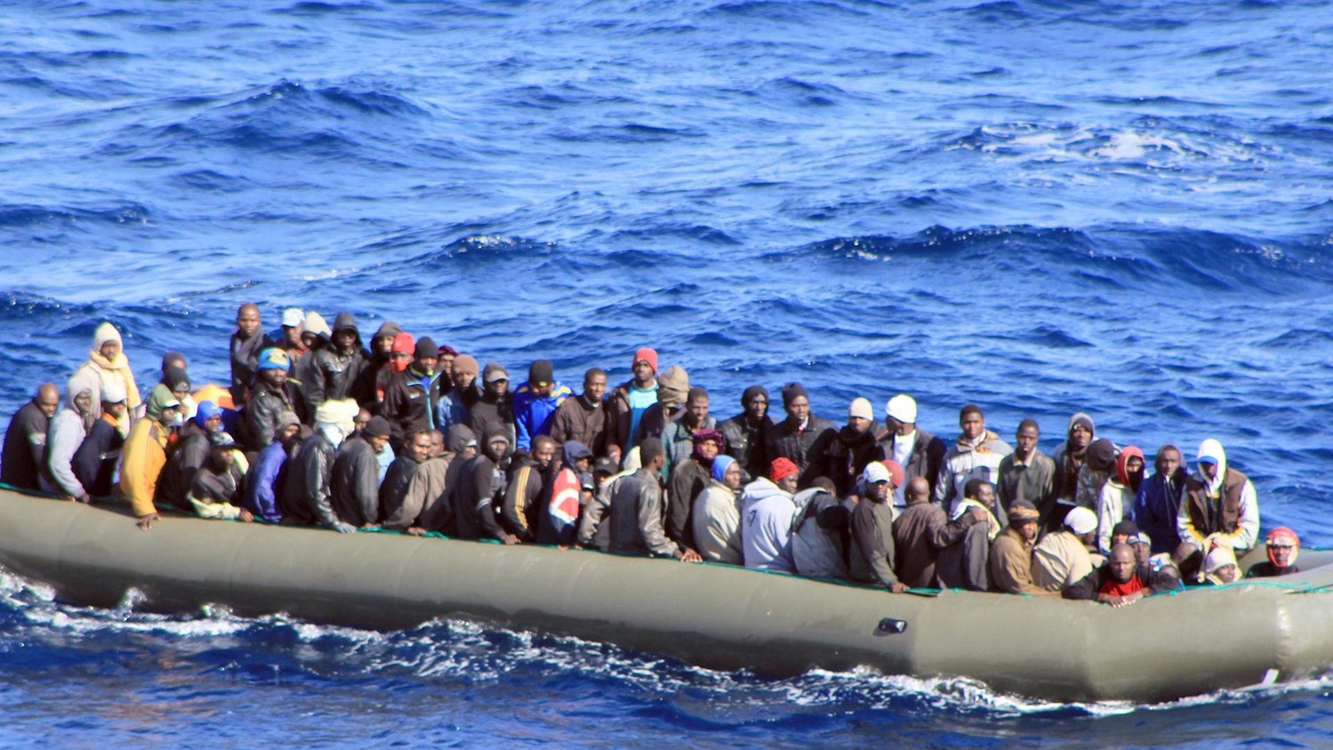 Ein überfülltes großes Schlauchboot mit mehreren Dutzend Menschen treibt auf dem Wasser.