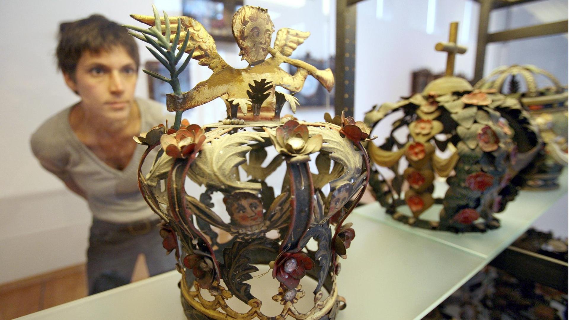 Eine Frau schaut in einem Museum in eine gläserne Vitrine, in der eine Krone steht.