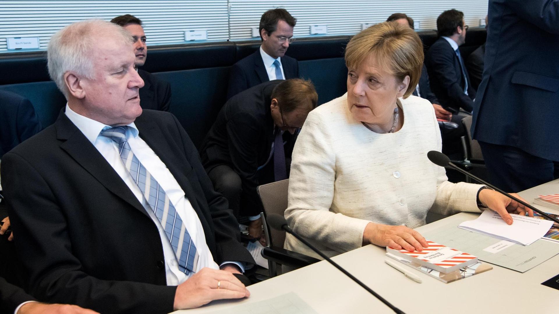 Seehofer (l) und Merkel (r) sitzen nebeneinander an einem Tisch und tauschen distanzierte Blicke. Seehofer (l) und Merkel (r) sitzen nebeneinander an einem Tisch und tauschen distanzierte Blicke.
