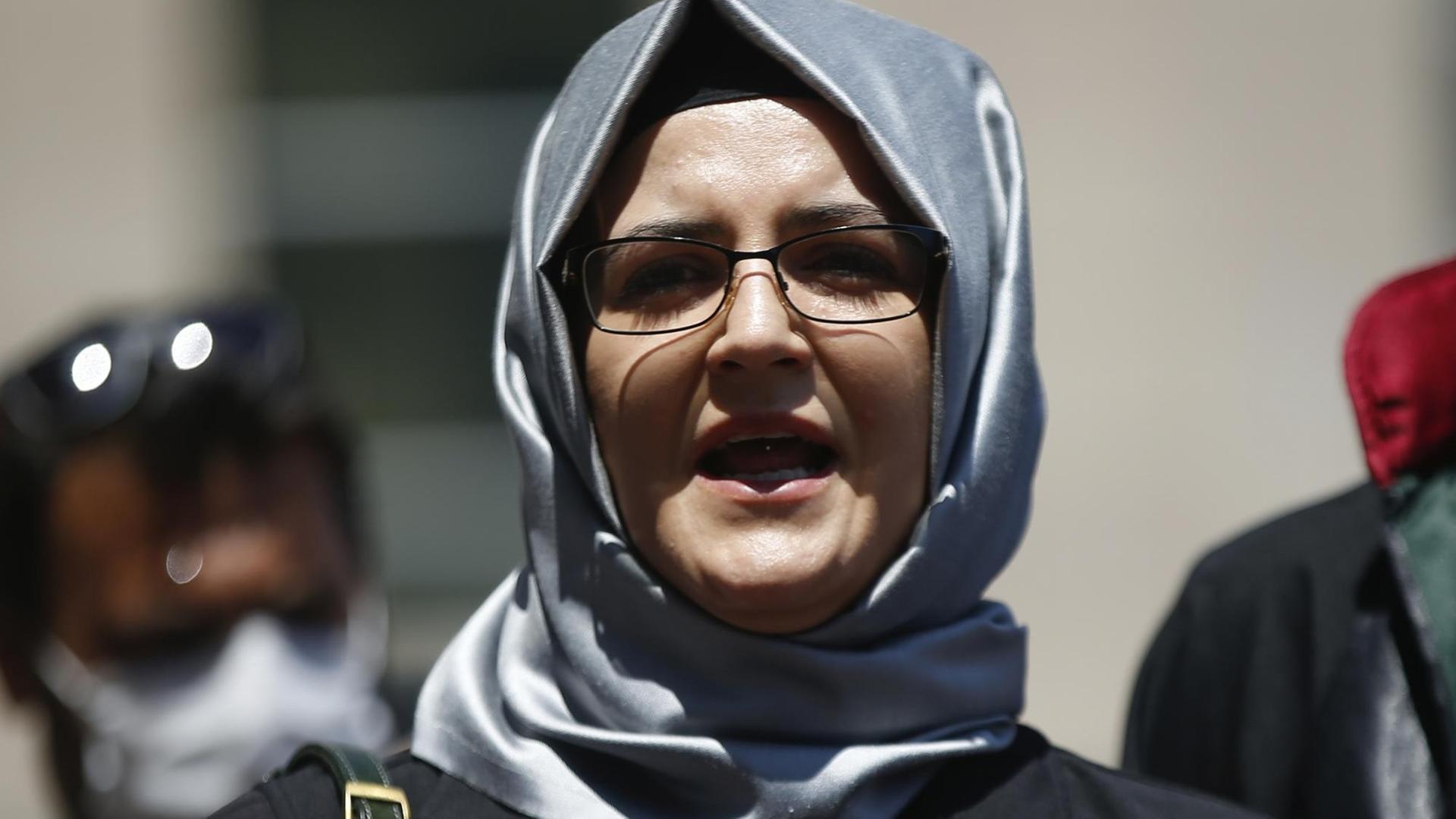 Hatice Cengiz – mit silbernem Kopftuch und schwarzer Brille – spricht in ein Mikrofon. Hatice Cengiz – mit silbernem Kopftuch und schwarzer Brille – spricht in ein Mikrofon.