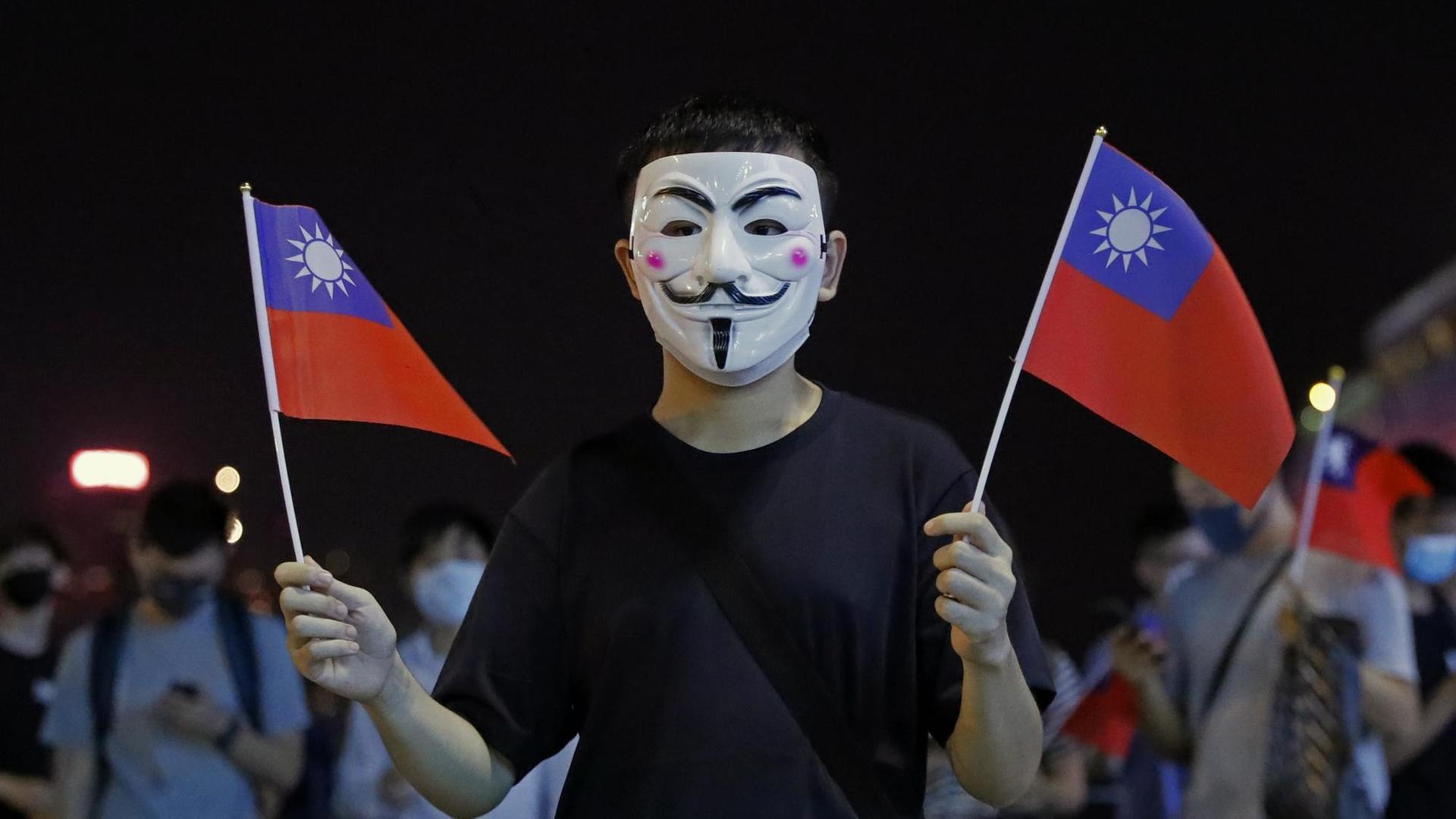 Ein Mann mit Maske hält bei einer Kundgebung für die Unabhängigkeit Taiwans am National Day Taiwans am 10.10.2019 zwei taiwanesische Flaggen. Ein Mann mit Maske hält bei einer Kundgebung für die Unabhängigkeit Taiwans am National Day Taiwans am 10.10.2019 zwei taiwanesische Flaggen.