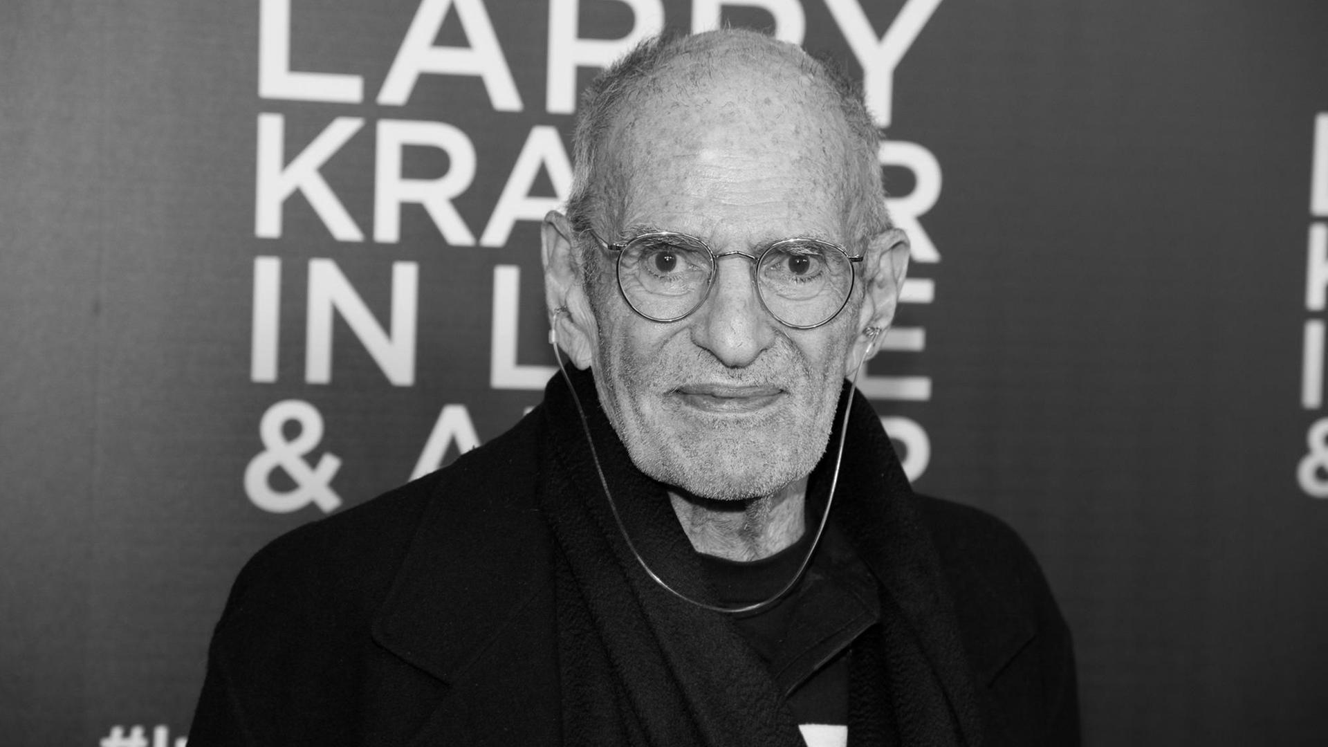 Larry Kramer steht vor einem Plakat mit seinem Namen und lächelt in die Kamera. Larry Kramer steht vor einem Plakat mit seinem Namen und lächelt in die Kamera.