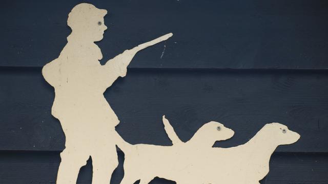 Auf einem Holzschnitt an einem Haus ist ein Jäger mit einem Gewehr und zwei Hunden zu sehen.