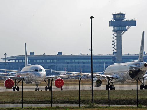 Lufthansa Maschinen parken auf dem Gelände des noch nicht eroeffneten Flughafens BER - im Hintergrund sind Terminal und Tower erkennbar.