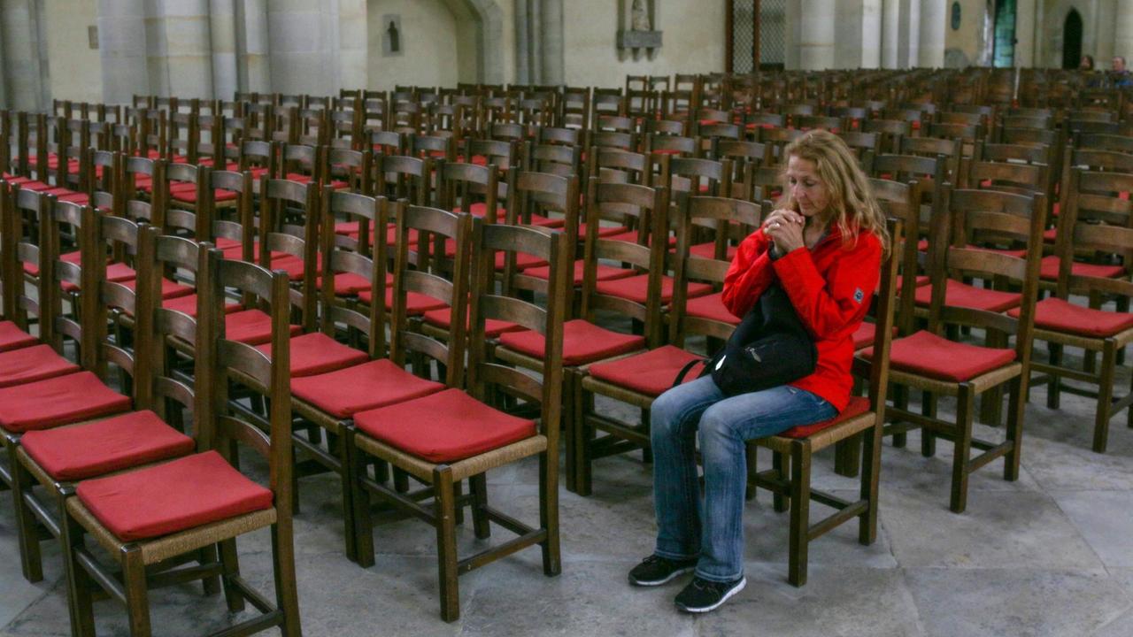 Frau sitzt im Magdeburger Dom inmitten leerer Stuhlreihen und betet. Frau sitzt im Magdeburger Dom inmitten leerer Stuhlreihen und betet.