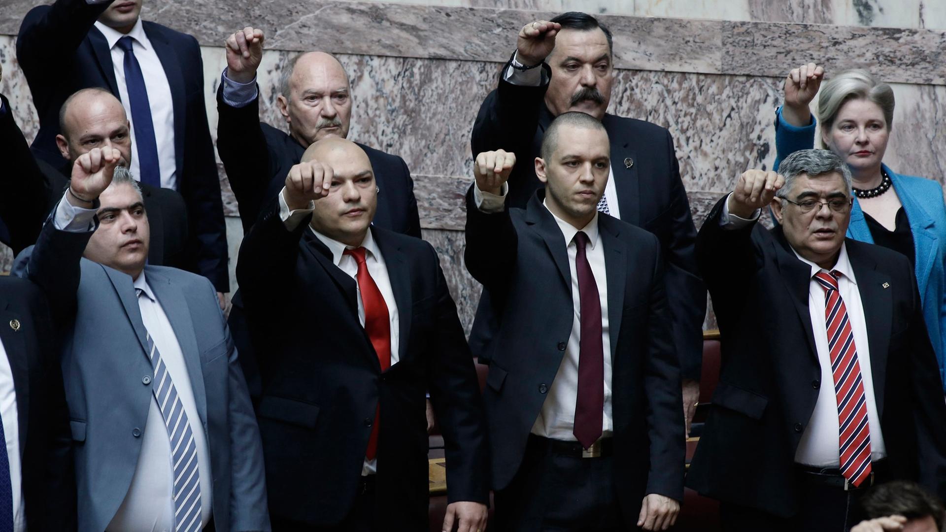 Nikolaos Michaloliakos, Parteichef der "Goldenen Morgenröte" (rechts) steht mit anderen Parteimitgliedern im griechischen Parlament, die rechten Hände in die Höhe gestreckt.