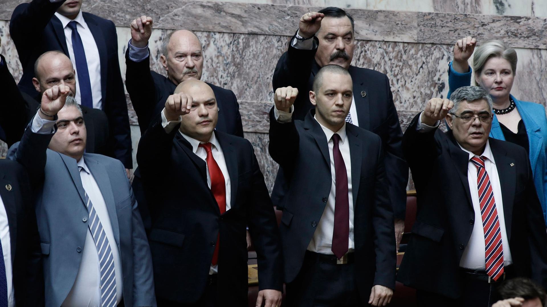 Nikolaos Michaloliakos, Parteichef der "Goldenen Morgenröte" (rechts) steht mit anderen Parteimitgliedern im griechischen Parlament, die rechten Hände in die Höhe gestreckt. Nikolaos Michaloliakos, Parteichef der "Goldenen Morgenröte" (rechts) steht mit anderen Parteimitgliedern im griechischen Parlament, die rechten Hände in die Höhe gestreckt.
