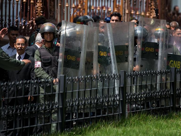 Streitkräfte Boliviens in Caracas (Venezuela) stehen an einem Zaun. Sie tragen Schutzschilde.