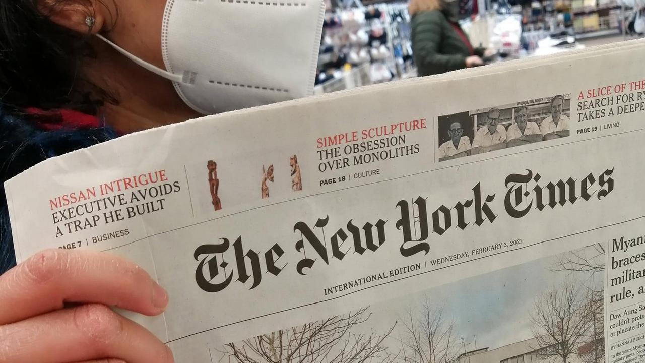 Eine Frau mit FFP2-Maske hält eine Printausgabe der "New York Times" in der Hand Eine Frau mit FFP2-Maske hält eine Printausgabe der "New York Times" in der Hand