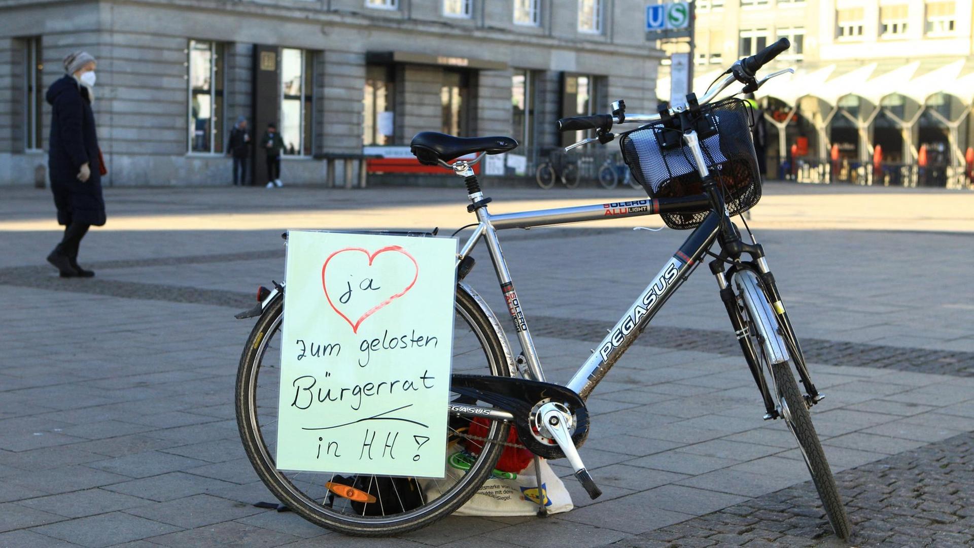Auf einem Fahrrad ist ein Zettel angebracht, der einen gelosten Bürgerrat in Hamburg fordert. Auf einem Fahrrad ist ein Zettel angebracht, der einen gelosten Bürgerrat in Hamburg fordert.