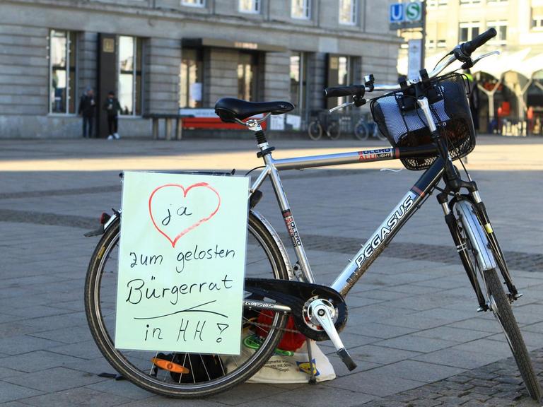 Auf einem Fahrrad ist ein Zettel angebracht, der einen gelosten Bürgerrat in Hamburg fordert.