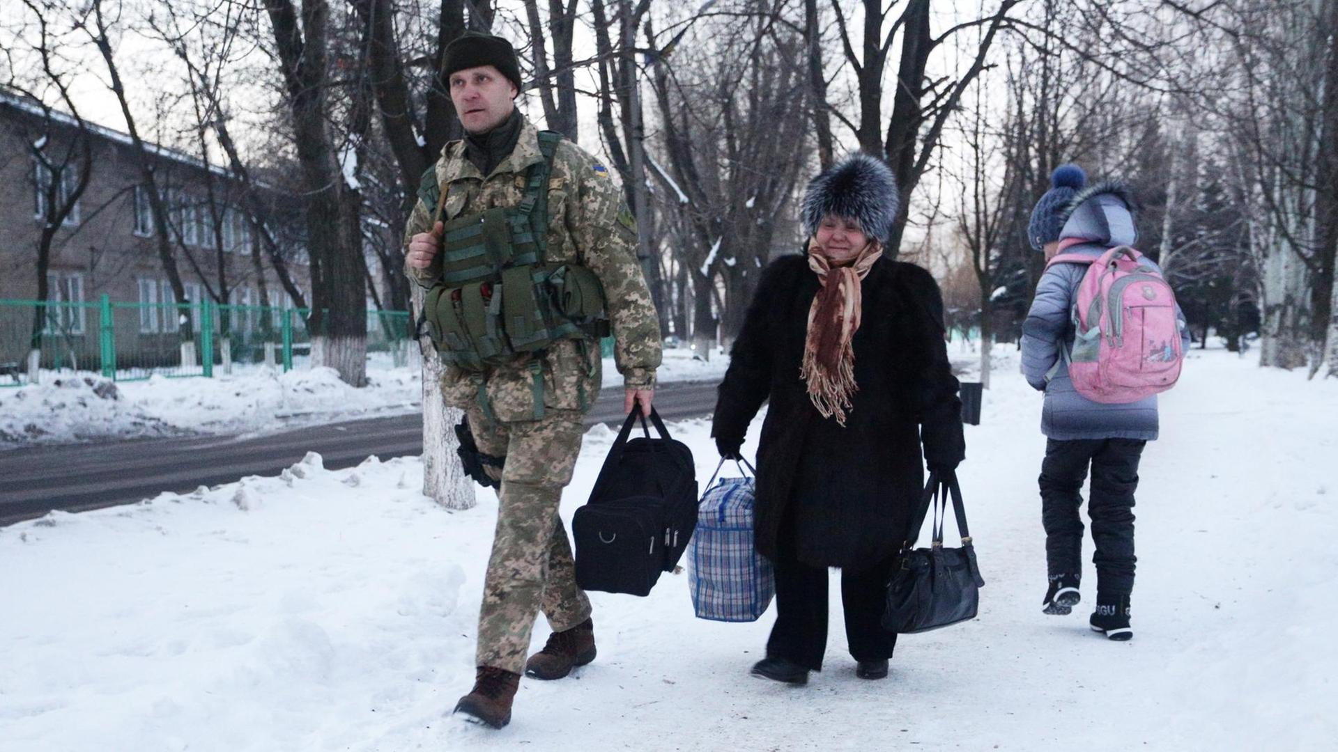 In Awdijiwka trägt ein ukrainischer Soldat die Sachen einer älteren Frau zu einem Versorgungszelt.