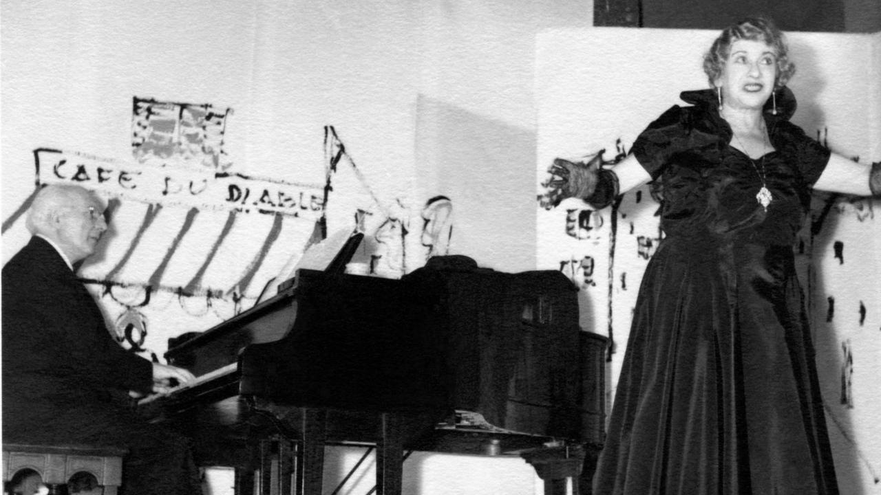 Auf einer historischen Fotografie singt eine Frau in dunklem Kleid auf einer Bühne, die von einem Pianisten begleitet wird.
