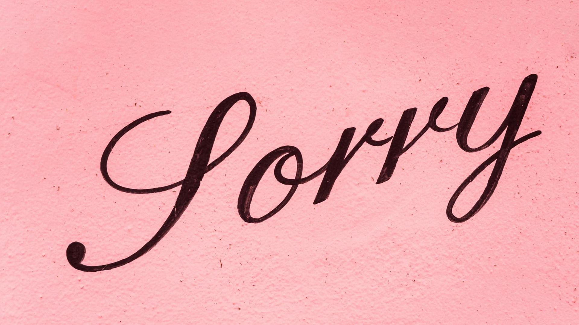 Auf einer rosafarbenen Hauswand steht in schwarzer Schreibschrift „Sorry” Auf einer rosafarbenen Hauswand steht in schwarzer Schreibschrift „Sorry”