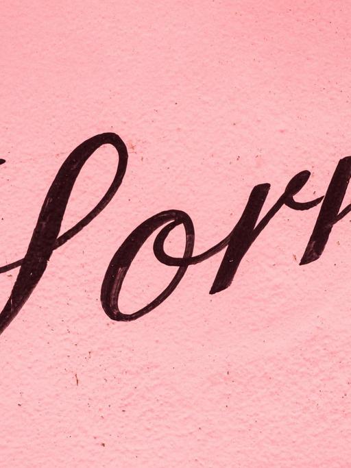 Auf einer rosafarbenen Hauswand steht in schwarzer Schreibschrift „Sorry”