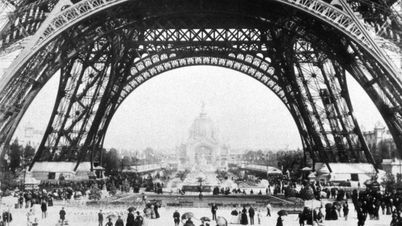 Ausstellungsbesucher der Weltausstellung in Paris 1889 wandeln unter dem Eiffelturm.