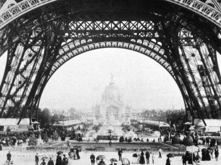 Ausstellungsbesucher der Weltausstellung in Paris 1889 wandeln unter dem Eiffelturm.