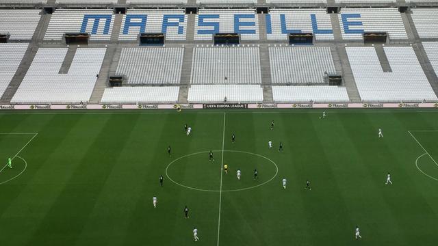 Die Fußballmannschaften von Olympique Marseille und Eintracht Frankfurt spielen, im Hintergrund eine leere Zuschauertribüne mit dem Schriftzug "Marseille".