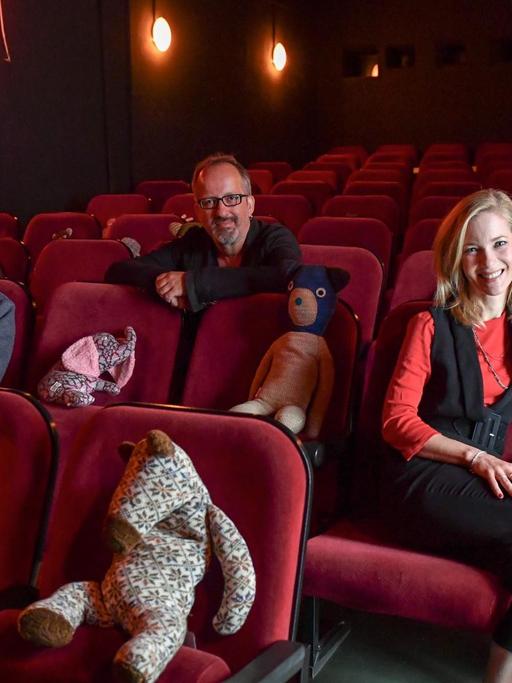 Sascha Grunow, Christos Acrivulis und Martina Klier (v.l.n.r.) sitzen im Kinosaal in roten Sesseln. Auf Sesseln dazwischen haben sie Kuscheltiere platziert.