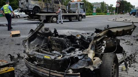 Arbeiter schleppen in der ost-ukrainischen Stadt Donezk einen ausgebrannten Minibus ab, der durch eine Explosion neben einem ebenfalls ausgebrannten Auto zerstört wurde.