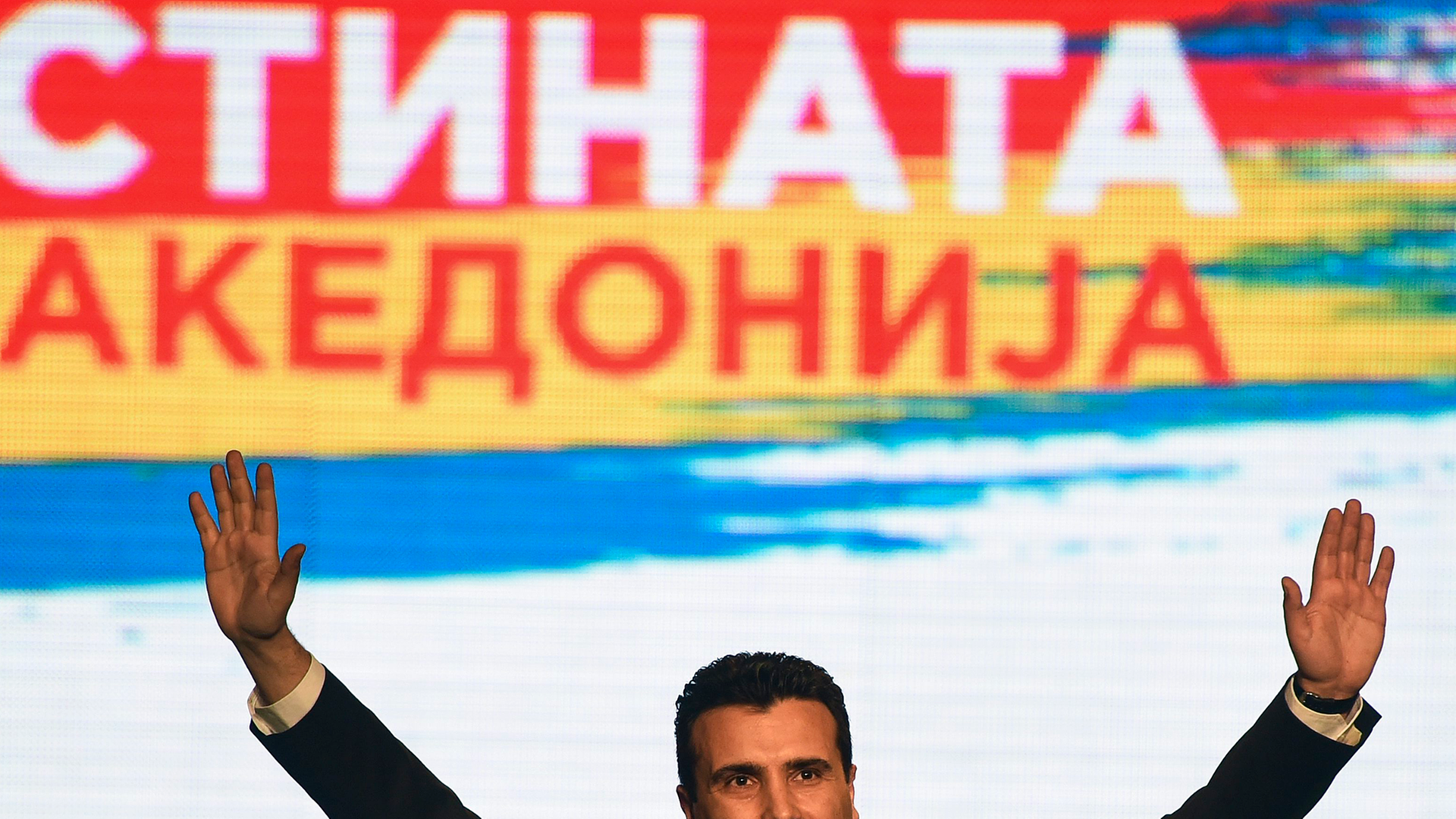 Zaef am 10. März 2015 in Skopje bei einer Rede auf einer Volksversammlung vor einem bunten Plakat. Um seine Worte zu betonen, hebt er beide Arme.