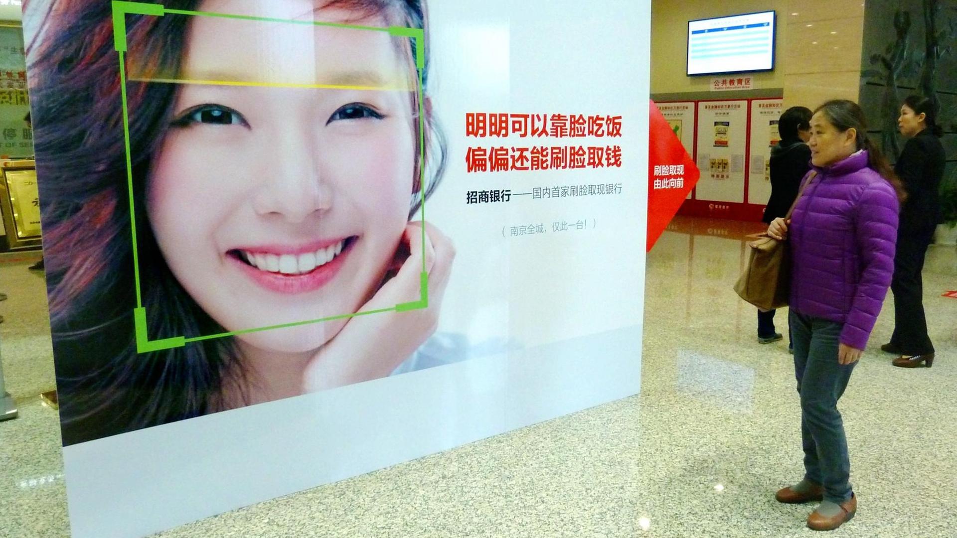 Eine Frau schaut in Nanjing in der Provinz Jiangsu auf ein Werbeplakat, das für das Geldabheben am Automaten per Gesichtserkennung wirbt Eine Frau schaut in Nanjing in der Provinz Jiangsu auf ein Werbeplakat, das für das Geldabheben am Automaten per Gesichtserkennung wirbt