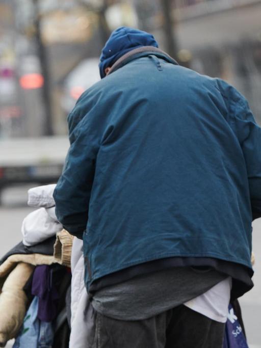 Eine obdachloser Mann läuft mit einem Einkaufswagen mit Jacken und Decken am Zoologischen Garten über die Straßen.