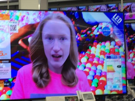 Das Gesicht der Künstlerin Britta Thie ist auf einem Flachbildschirm-Fernseher zu sehen, der in einem Elektrofachhandel steht