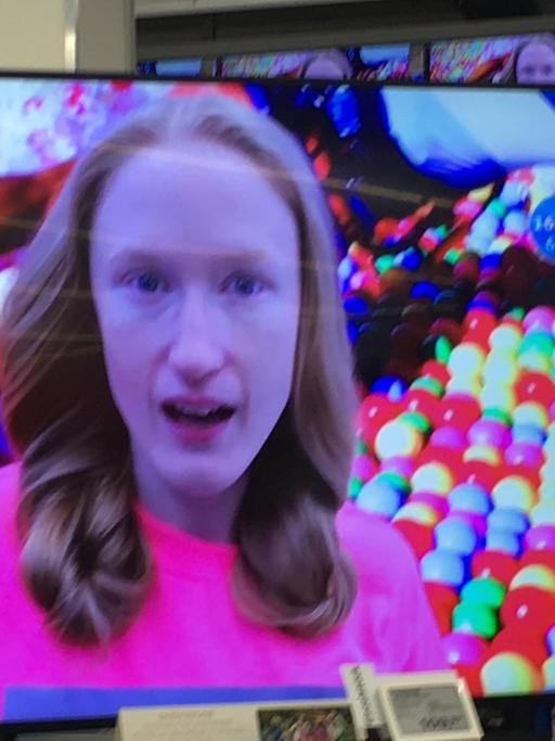 Das Gesicht der Künstlerin Britta Thie ist auf einem Flachbildschirm-Fernseher zu sehen, der in einem Elektrofachhandel steht