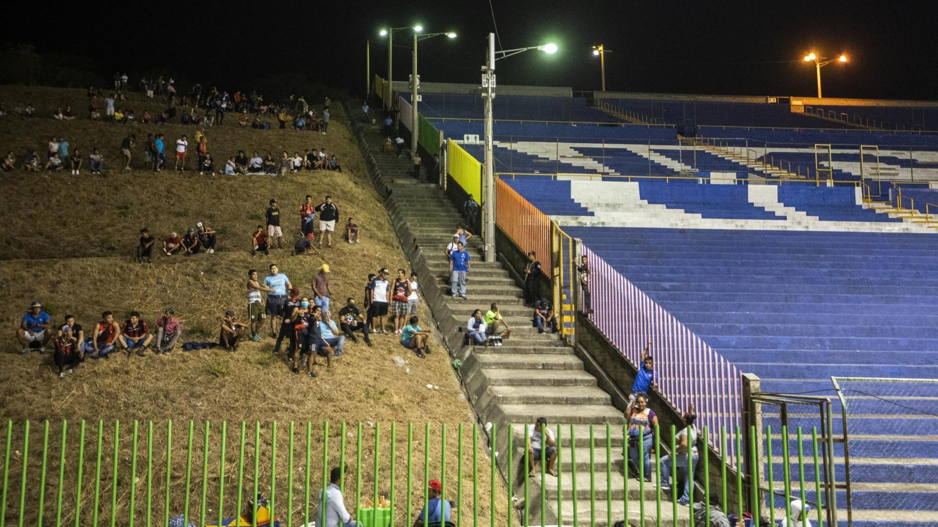 Ausserhalb eines leeren Fussballstadion sitzen Menschen auf der Wiese.