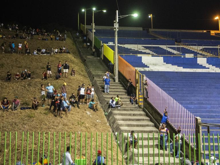 Ausserhalb eines leeren Fussballstadion sitzen Menschen auf der Wiese.