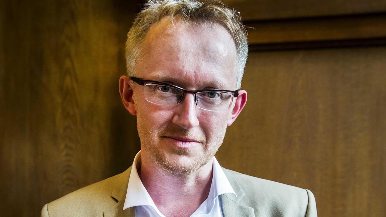 David van Reybrouck steht mit dem Preis in der Hand gegen eine Wand gelehnt. David van Reybrouck steht mit dem Preis in der Hand gegen eine Wand gelehnt.