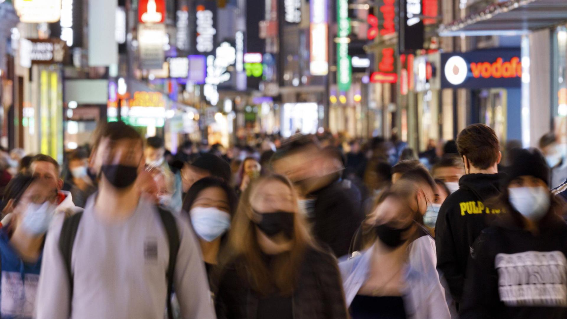 Menschen gehen mit Masken durch eine Fußgänger-Zone. Menschen gehen mit Masken durch eine Fußgänger-Zone.