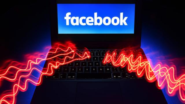 Auf dem Monitor eines Laptops, in den rote elektrische Blitze einschlagen, steht "facebook".