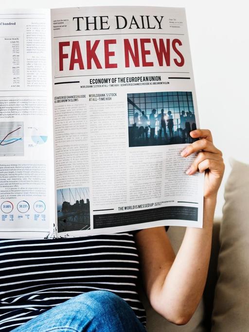 Eine Frau sitzt auf einem Sofa und liest die Zeitung "The Daily Fake News".