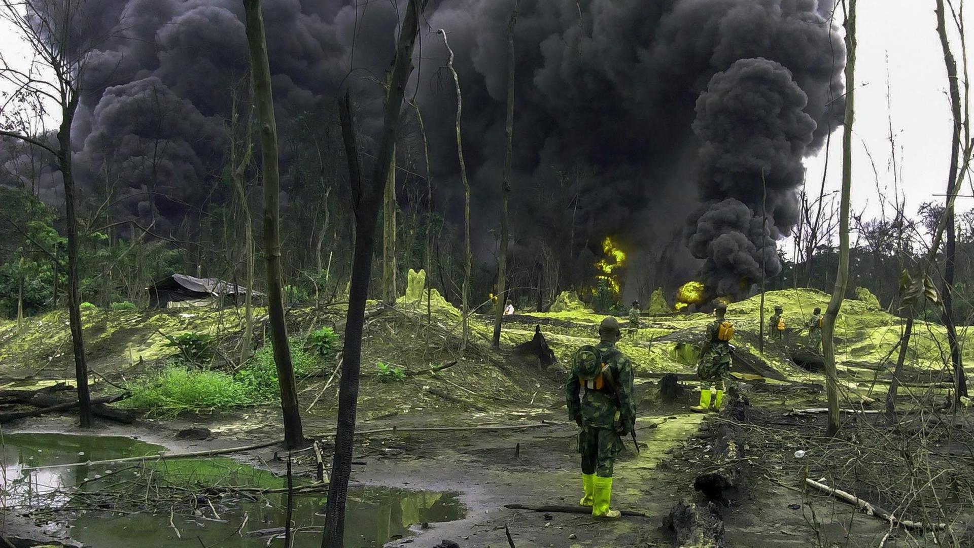 Nigerianische Soldaten stehen in einem Öl-verseuchten Gebiet im Niger-Delta und sehen eine große schwarze Wolke. Nigerianische Soldaten stehen in einem Öl-verseuchten Gebiet im Niger-Delta und sehen eine große schwarze Wolke.