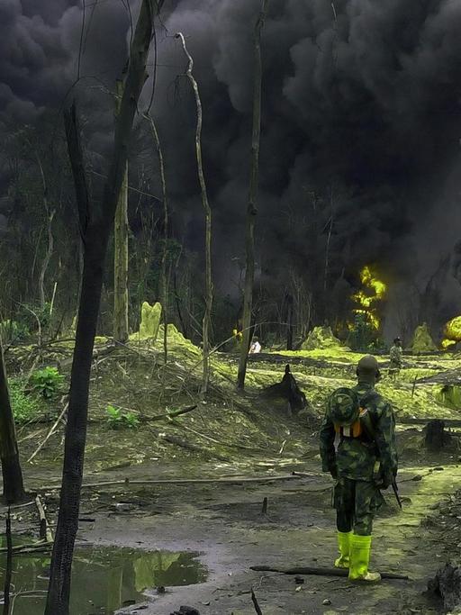 Nigerianische Soldaten stehen in einem Öl-verseuchten Gebiet im Niger-Delta und sehen eine große schwarze Wolke.