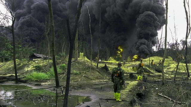 Nigerianische Soldaten stehen in einem Öl-verseuchten Gebiet im Niger-Delta und sehen eine große schwarze Wolke.