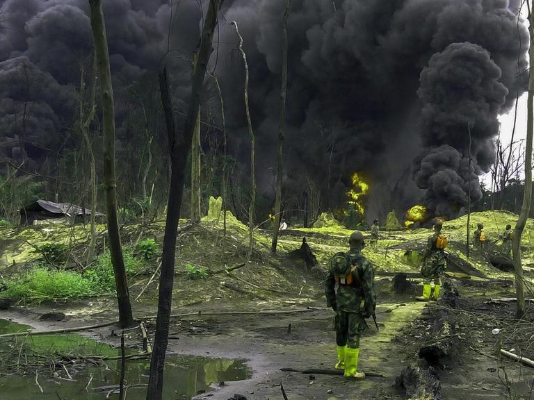 Nigerianische Soldaten stehen in einem Öl-verseuchten Gebiet im Niger-Delta und sehen eine große schwarze Wolke.