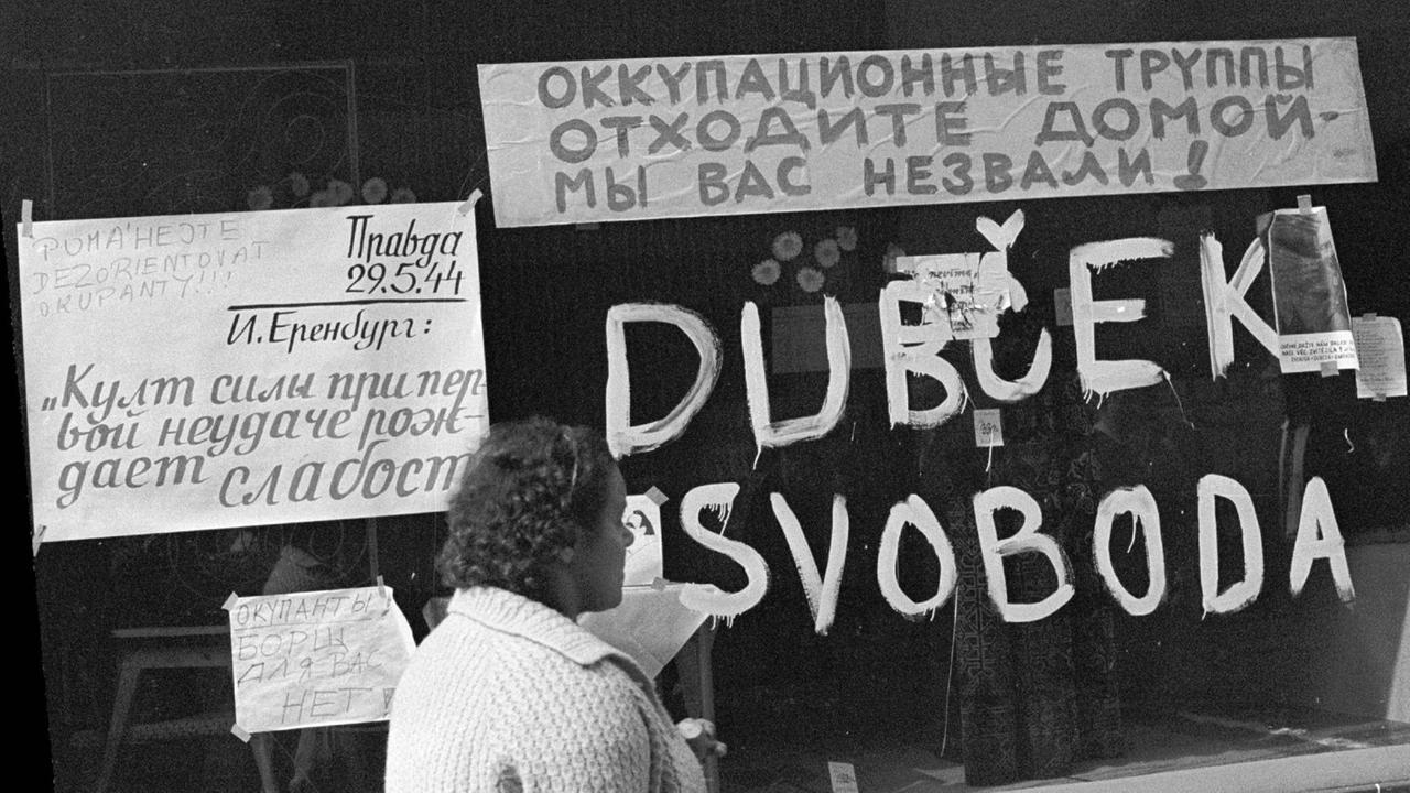 Eine Frau geht an einem Schaufenster vorbei, auf dem der Name "Dubcek" und das Wort "Svoboda" (Freiheit) stehen.