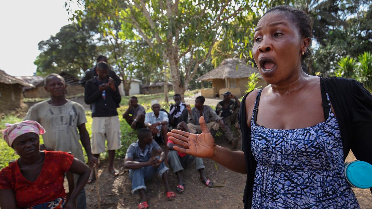 Eine klagende Frau in einem Dorf in Liberia, hinter ihr sitzen ein Dutzend Menschen Eine klagende Frau in einem Dorf in Liberia, hinter ihr sitzen ein Dutzend Menschen