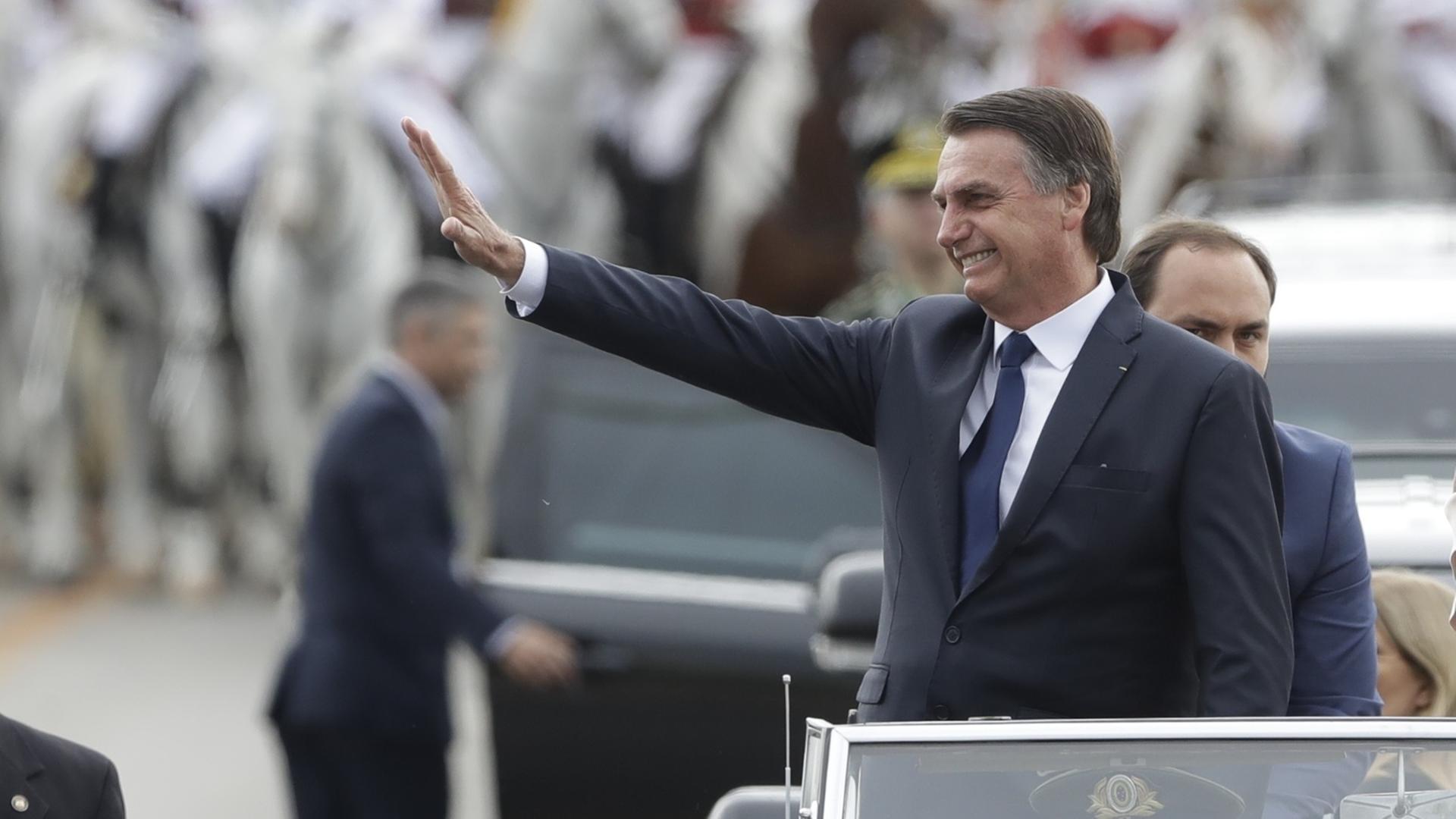 Das Bild zeigt Brasiliens neuen Präsidenten Jair Bolsonaro. Er steht in einem offen fahrenden Auto und winkt Anhängern zu. Das Bild zeigt Brasiliens neuen Präsidenten Jair Bolsonaro. Er steht in einem offen fahrenden Auto und winkt Anhängern zu.