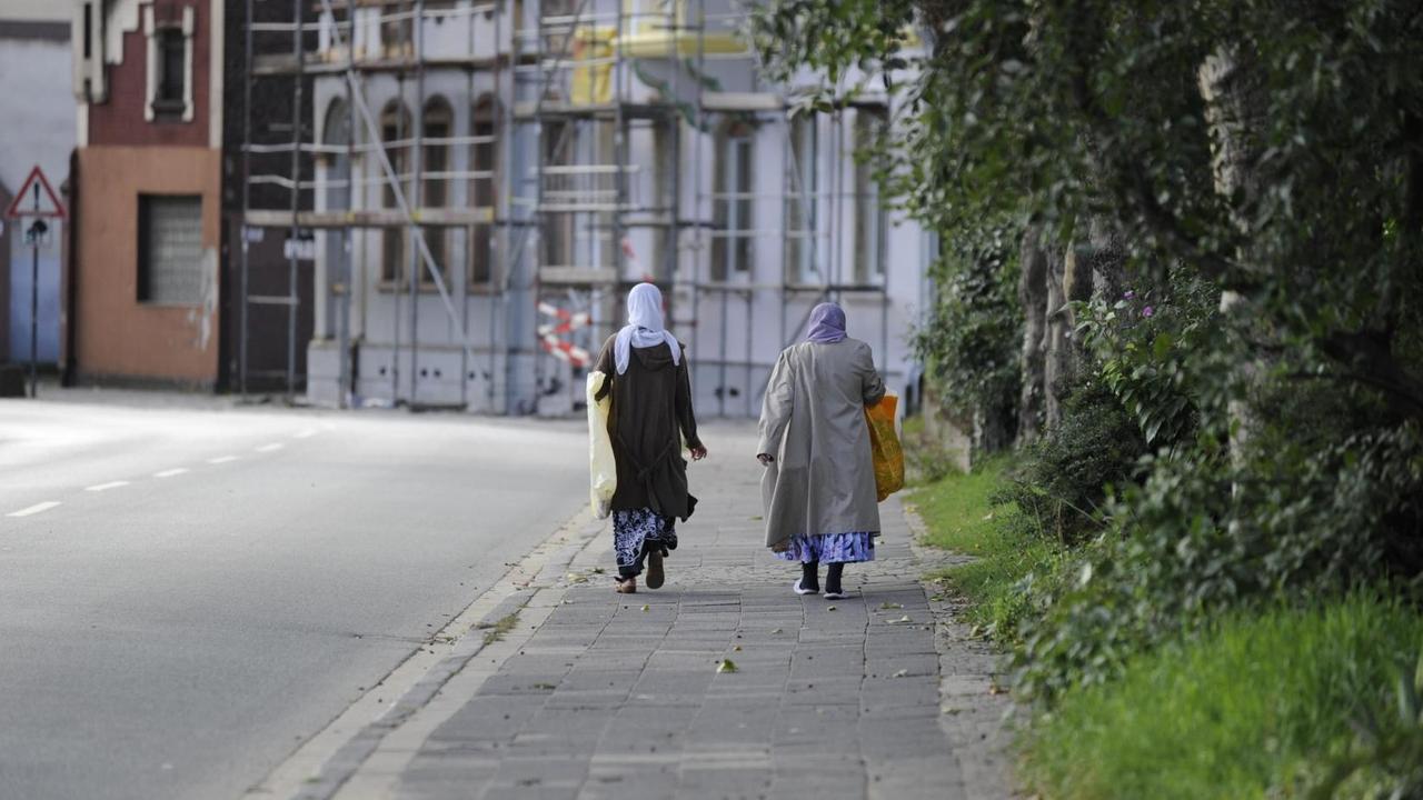 Das Bild zeigt zwei muslimische Frauen in weiterer Distanz auf einem Gehweg entlang laufen. Das Bild zeigt zwei muslimische Frauen in weiterer Distanz auf einem Gehweg entlang laufen.