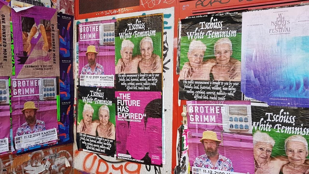 An der Wand sind viele gleiche Plakate zu sehen. Das Motiv zeigt zwei unbekleidete Frauen, zu sehen bis kurz vor Brusthöhe, die sich umarmen. Über ihren Köpfen steht "Tschüss, White Feminism" An der Wand sind viele gleiche Plakate zu sehen. Das Motiv zeigt zwei unbekleidete Frauen, zu sehen bis kurz vor Brusthöhe, die sich umarmen. Über ihren Köpfen steht "Tschüss, White Feminism"