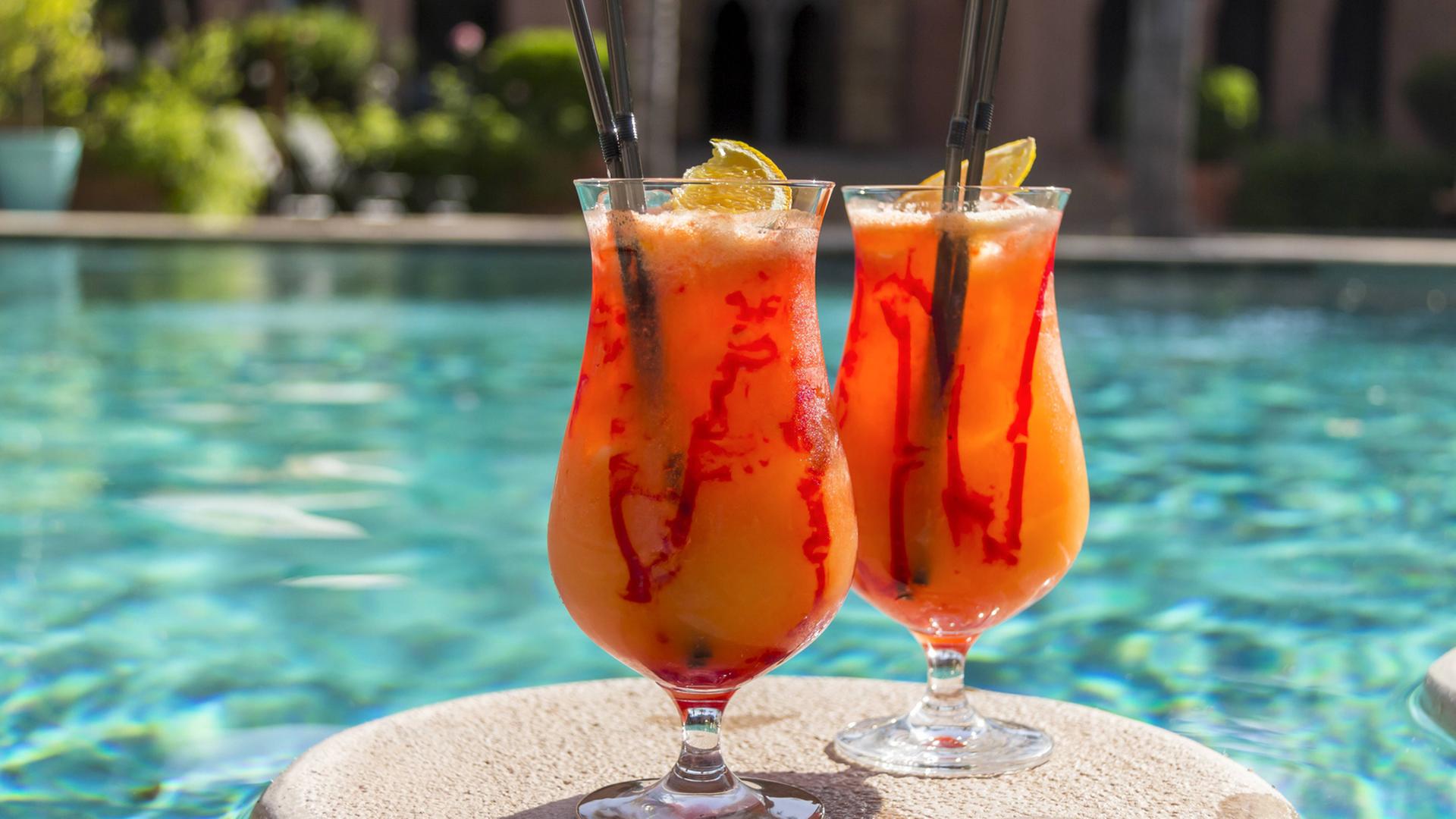 Zwei orange-rote Cocktails schwimmen auf einer Unterlage in einem Swimmingpool. Zwei orange-rote Cocktails schwimmen auf einer Unterlage in einem Swimmingpool.